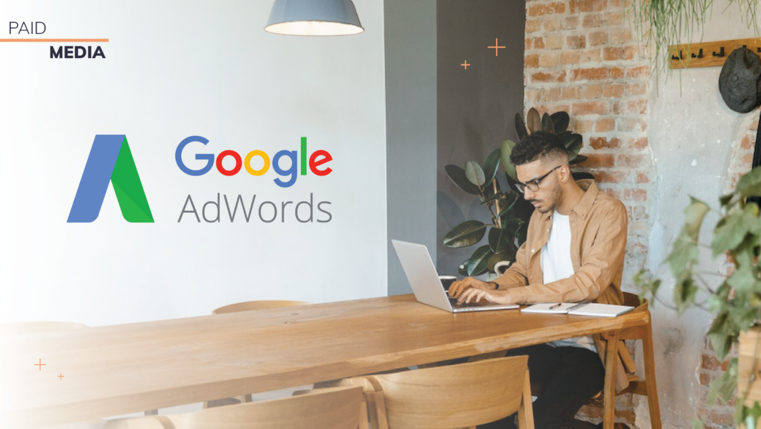 Man sitting at desk looking at laptop. Google Adwords logo imposed on the left side corresponding to blog article about "How to Audit an AdWords Campaign"