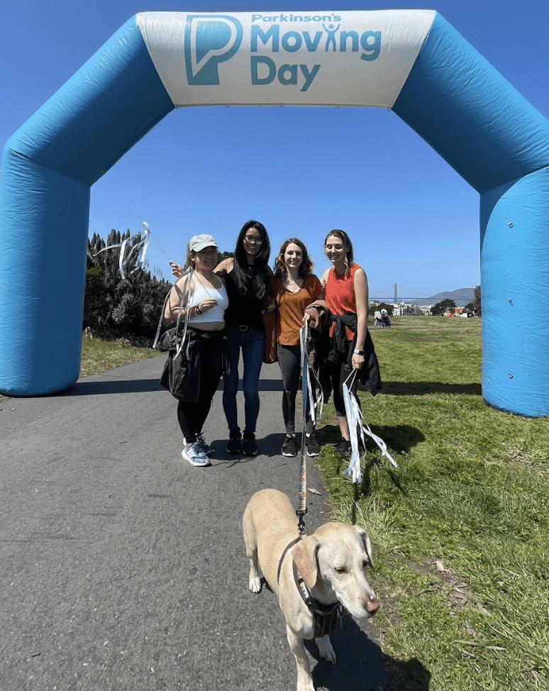 Four women and a dog in front of Parkinson's Moving Day Sign