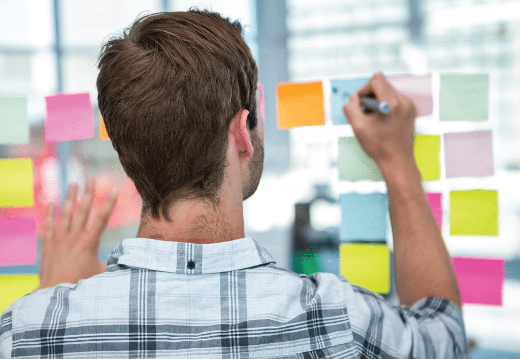 person writing on sticky notes on glass window