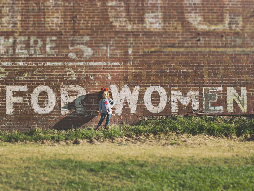 little girl standing in front of mural on building that says "for women"